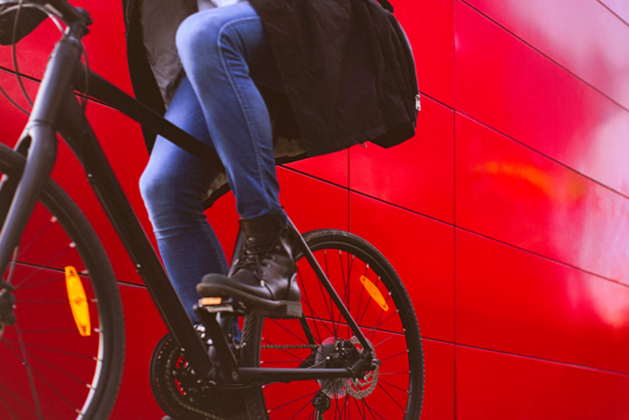 Handsome man, on the way to work, riding bicycle beside the red wall  The man is casually dressed and wears eyeglasses and carries black briefcase hung on shoulder  Motion concept, motion blur, copy space has been left 